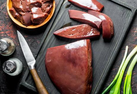 Beef liver on a black cutting board being prepared for cooking by cutting into chunks.