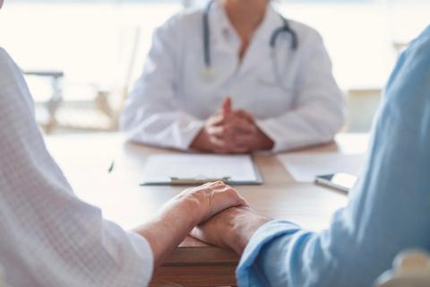 Couple holding hands on one side of desk, with doctor on the other side