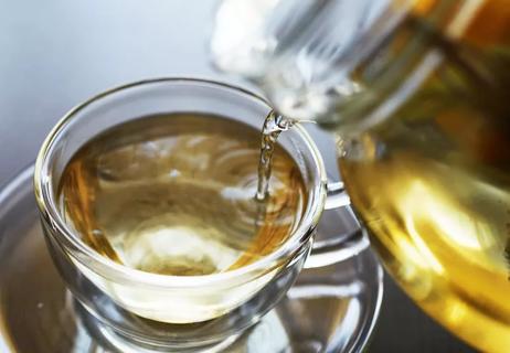 Someone pours hot tea into a small, glass tea cup.