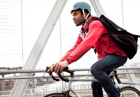 Person wearing bicycle helmet riding bike to work over bridge.