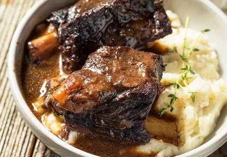 Bowl of braised short ribs with fennel seed and apple cider vinegar on a bed of mashed potatoes