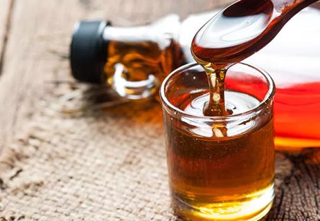 A wooden spoon in a glass jar of maple syrup