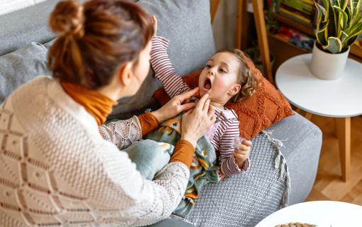 Toddler lying on couch, with caregiver checking toddler's throat