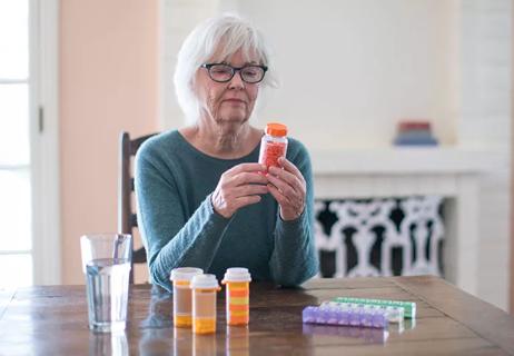 A person wearing glasses sitting at a table reading medication bottles