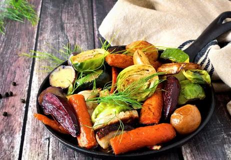 Roasted carrots and brussel sprouts in a cast iron page on a wooden table.