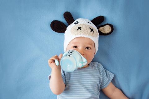 Baby lying down with crocheted cow hat on, drinking from sippy cup