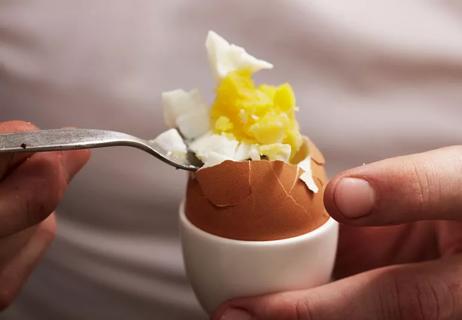 Person eating a poached egg out of an egg cup holder.