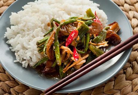 Plate of Thai green beans and white rice on a blue plate with wooden chopsticks