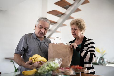Older couple unpacking groceries from paper bag, examining the bananas