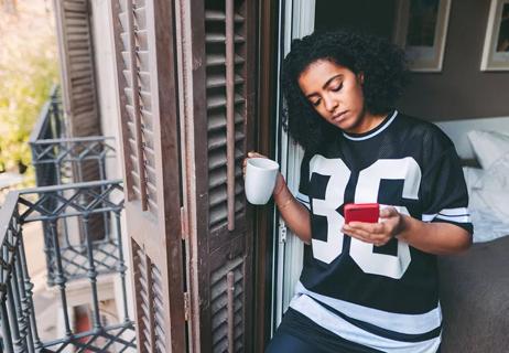 Woman sheltering in place drinking coffee and checking phone while at home