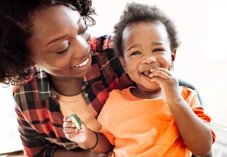 Toddler eating cucumbers in mother's arms