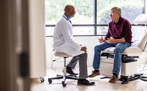 Older male in doctor's office sitting on exam chair, talking with healthcare provider