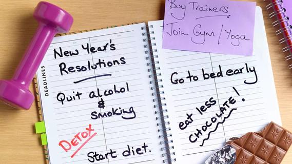 various New Year's resolutions written in date planner, with weights and chocolate in foreground