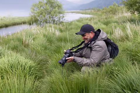 Person enjoying outdoor photography, in tall grass by a river