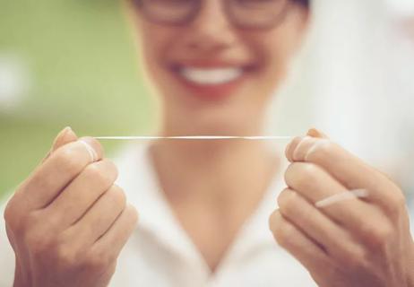 An individual smiles while holding dental floss