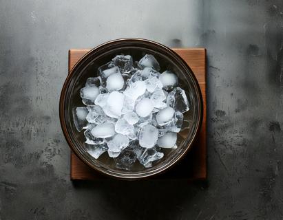 Metal bowl of icecubes on wooden block on table