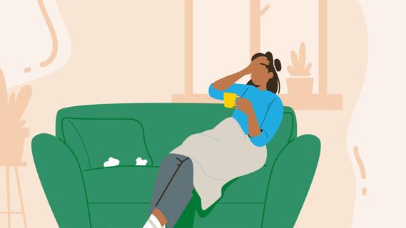Person sitting on couch, hand on head, wrapped in blanket, holding hot beverage, used tissues nearby
