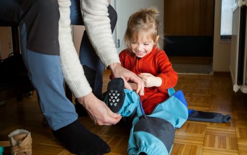 Caregiver helping happy child put on snow pants