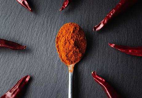 A spoon full of cayenne pepper surrounded by peppers.