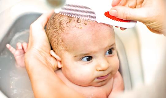 Caregiver giving newborn a bath, gently removing cradle cap with comb