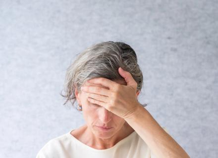 Older woman with gray hair with head bent down and hand on forehead, looking pensive