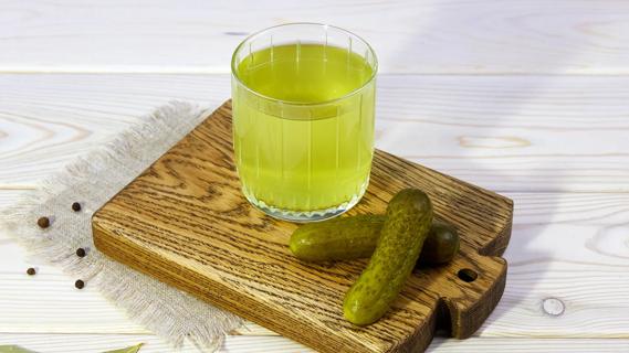 Pickle juice in a glass on a wooden board with pickles