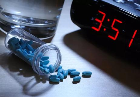 sleeping pills on bedside table with clock and glass of water