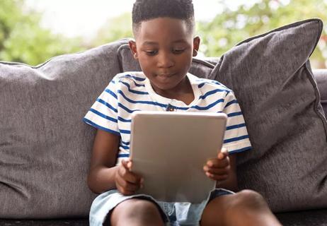 Child sitting on beige couch using tablet to access the internet.