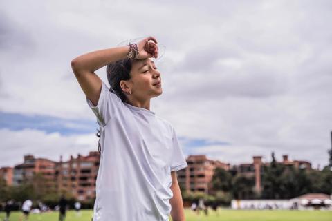 Kid outside on soccer field, wiping forehead