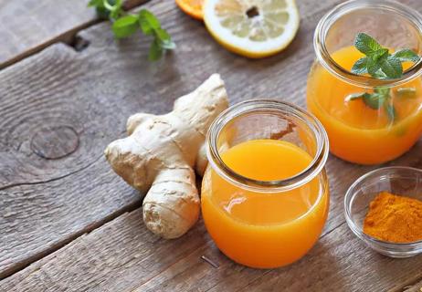 Ginger mixed with orange juice to produce a ginger shot shown on a wooden table.