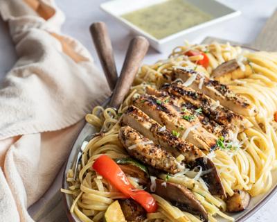 Platter of grilled chicken and vegetables over linguine