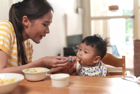 Caregiver spoon feeding baby in highchair at the table