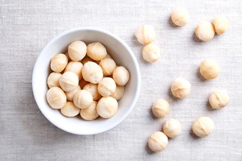 White bowl of whole, shelled macadamia nuts, with a few scattered on table