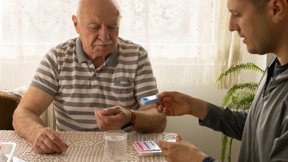 older man at a table with younger man handing him pill containers