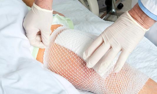 Hands of healthcare provider checking bangages on knee after surgery