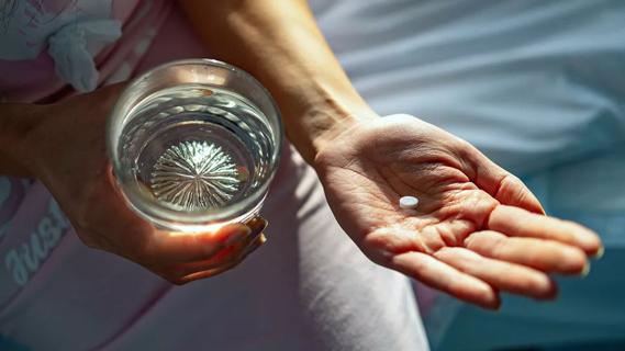 Closeup of hands holding a glass of water and an aspirin