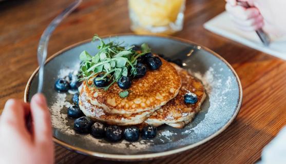 Person about to eat a plate full of pancakes with blueberries on top