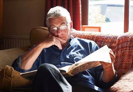 Man serious and alone on sofa contemplating magazine