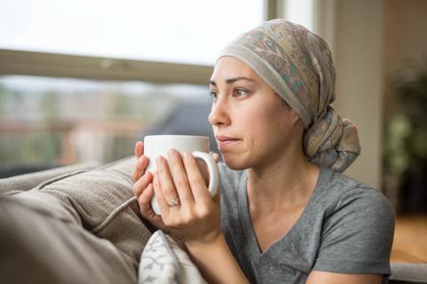 Woman sitting on the couch with head scarf on, holding a mug of tea, staring out the window