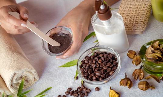 Hands mixing ground coffee beans and lotion for a face mask