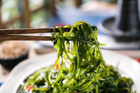 Chopsticks picking up bite of seaweed from a plate