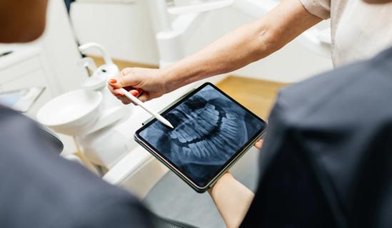 Dental care provider holding tablet showing X-ray image, pointing out part of the