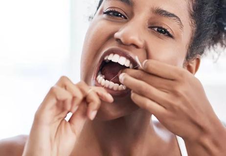 Person flossing teeth with a long piece of floss wrapped around their fingers.