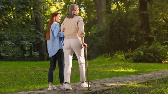 Woman helping older woman as she walks with a cane
