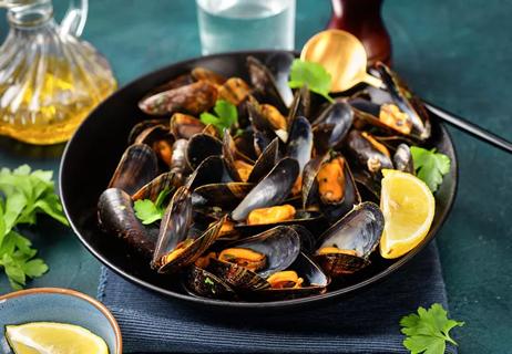 Cooked mussels with a lemon and herb garnish in a black bowl