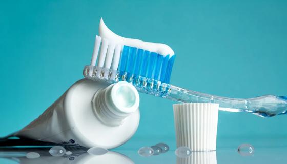 Open tube of toothpaste, with toothbrush resting against it, with the cap nearby