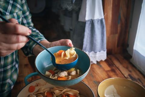 Person ladling chicken noodle soup into a bowl