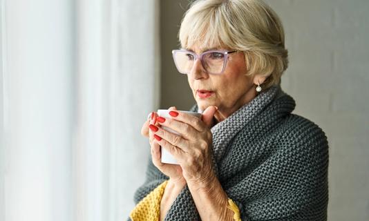 Fashionable older person blowing into a mug, looking out window