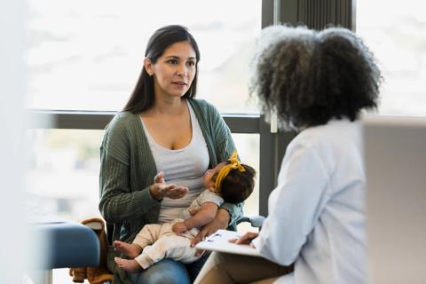 Caregiver holding baby while talking with a healthcare provider in medical office