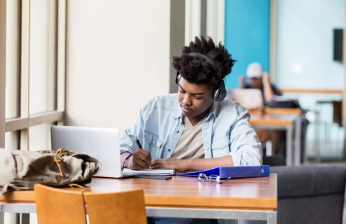 Person studying with headphones on, with laptop and notepad